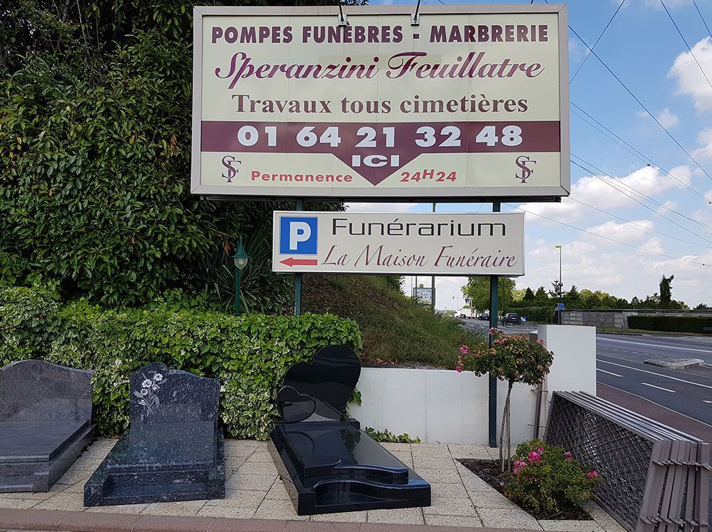 Monument funéraire avec pierres tombales, panneau gravé et panneau de stationnement en bord de route.