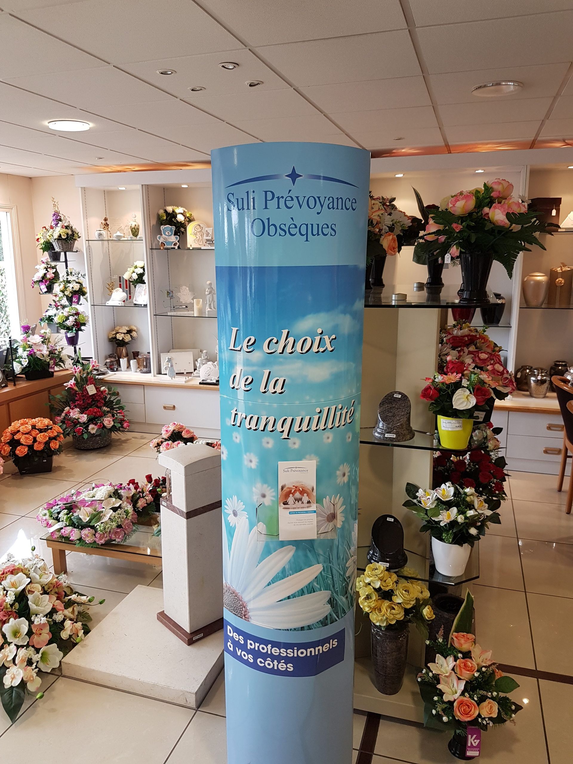 Allée d'un magasin de fleurs avec des compositions florales aux tons pastel et une bannière publicitaire bleue en guise de centre de table