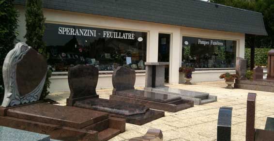 Mémorial extérieur composé de plusieurs plaques et monuments en pierre devant un bâtiment portant l'inscription « Sprainin Funeral Home ».