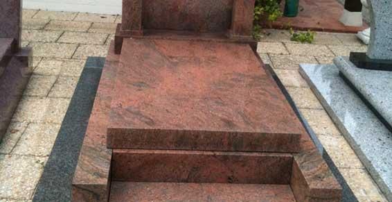Un monument commémoratif en pierre rouge avec une petite marche, situé parmi d'autres tombes sur une allée pavée.