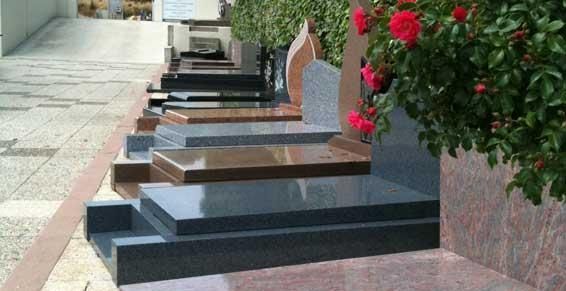 Une rangée de tombes en granit poli borde un trottoir, avec des fleurs rouges près d'un monument.