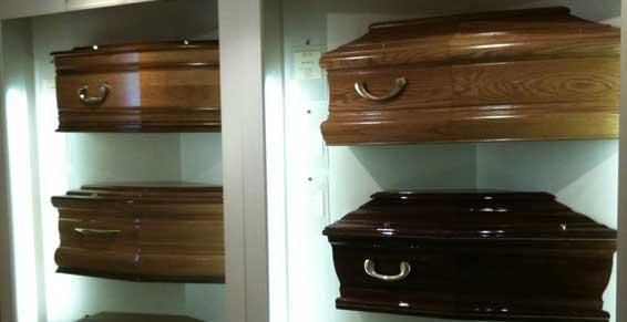 Quatre cercueils en bois sont exposés dans une pièce intérieure blanche, deux brun clair et deux brun foncé.