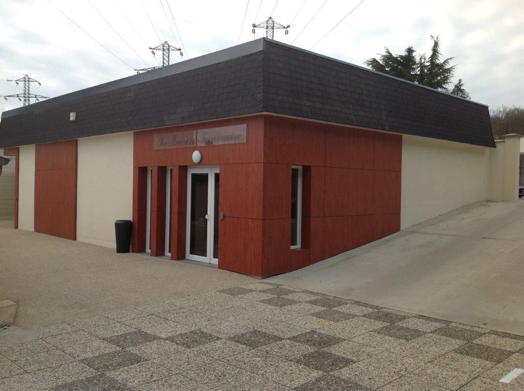 Petit bâtiment rouge à façades blanches et toit noir sur un terrain gravillonné