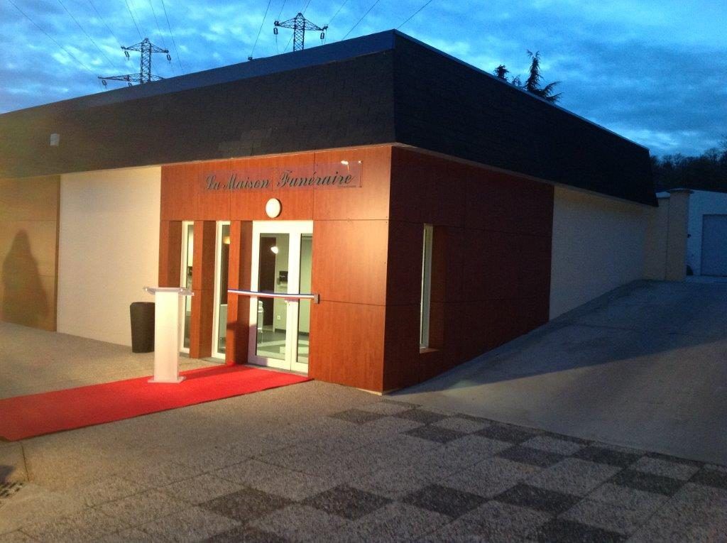 Entrée d'un immeuble moderne avec tapis rouge, porte illuminée et ciel bleu du soir