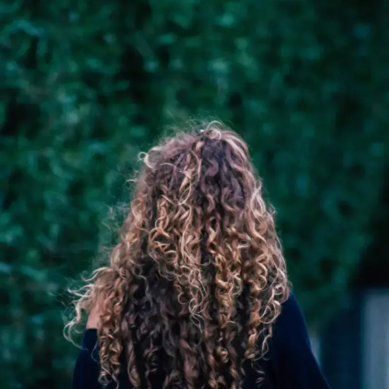 Mujer con cabello rizado moviendo la cabeza, al aire libre, luz del sol.