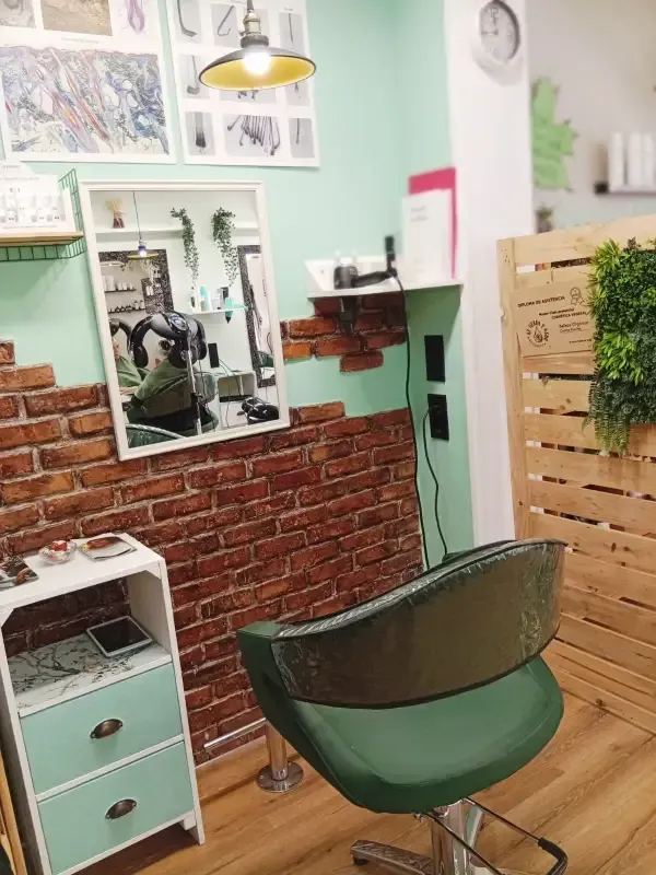 Interior de salón con pared de ladrillo, armario y silla de color verde menta y una mampara de madera decorativa.