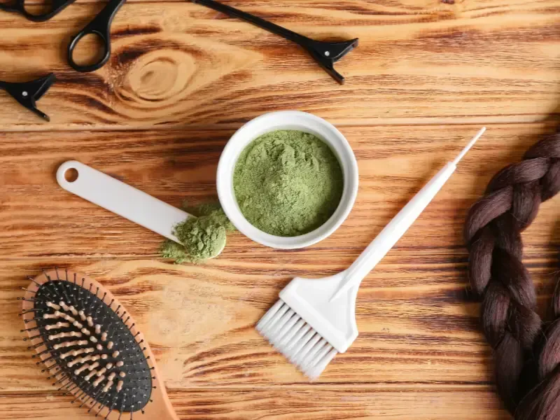 Herramientas para teñir el cabello: recipiente con polvo verde, cepillo, pala, peine, tijeras, pinzas para el cabello.