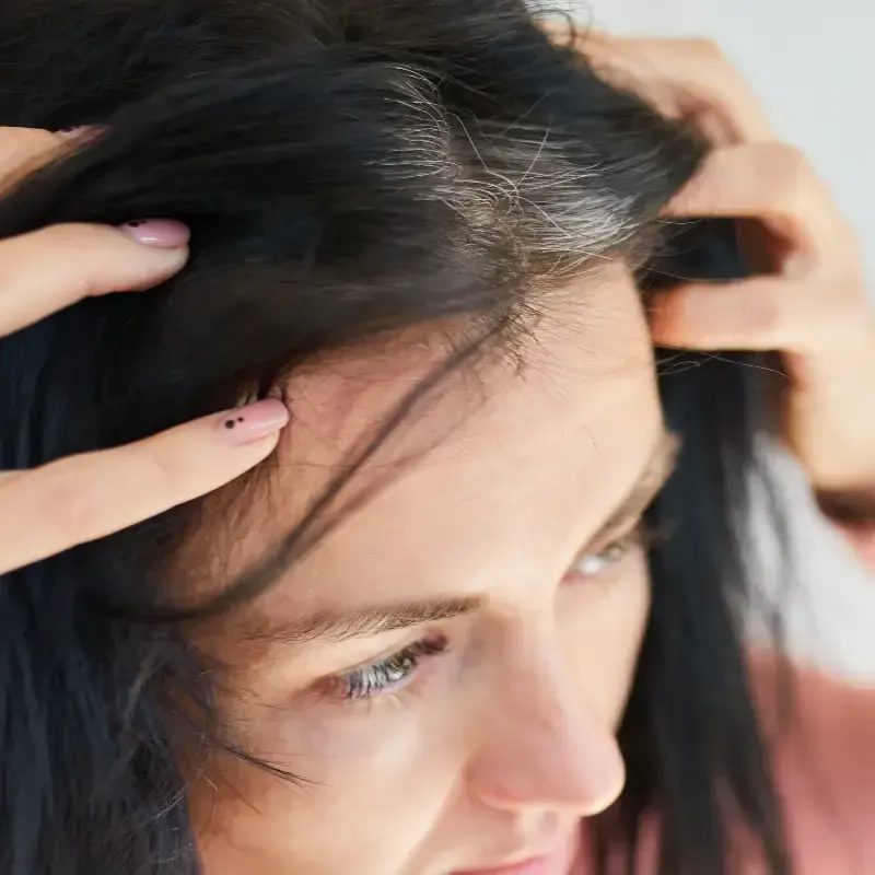 Mujer revisando su cabello oscuro en busca de raíces grises.