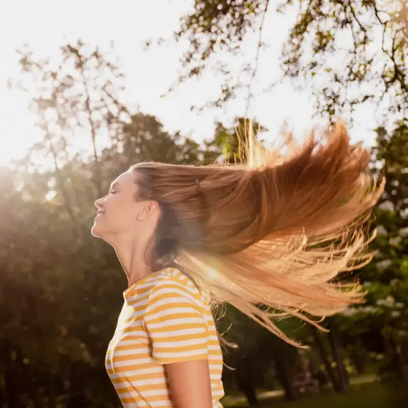 Mujer con cabello largo y rojo y lápiz labial rojo, ojos cerrados, descansando sobre follaje verde.
