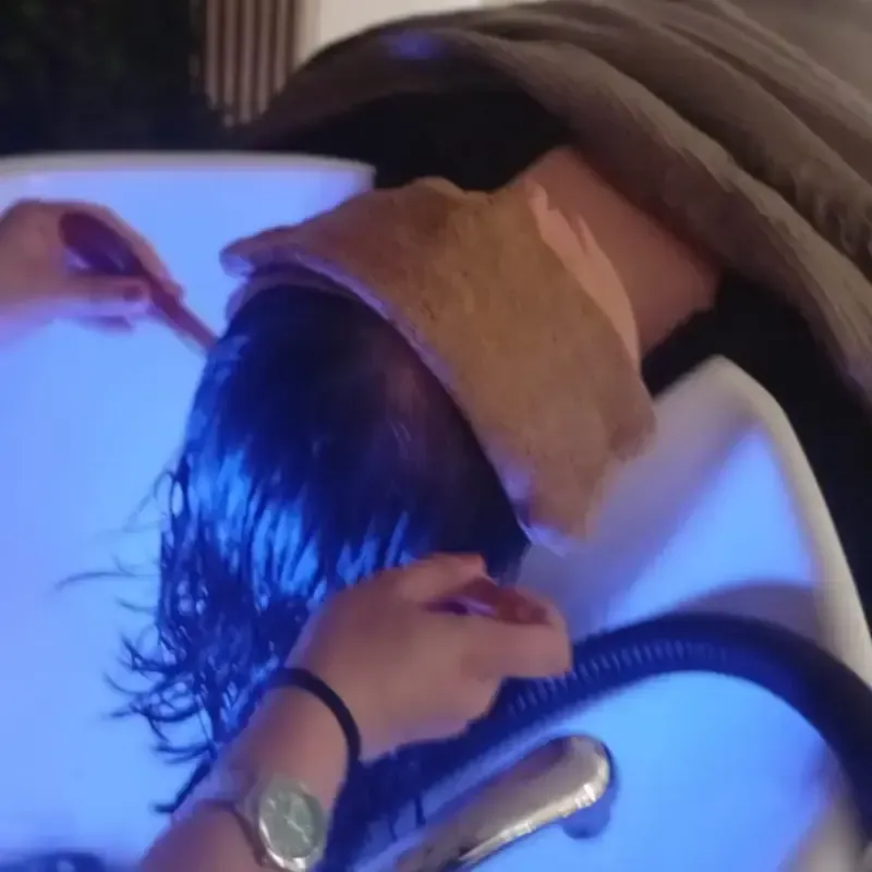 Mujer recibiendo masaje facial, ojos cerrados, manos en la cara, diadema blanca, esmalte de uñas rojo.