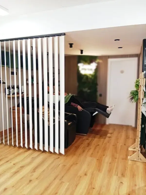 Biombo divisorio de listones blancos con una persona reclinada en una silla negra en un entorno tipo spa.