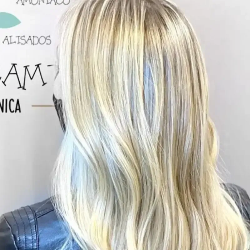 Cabello rubio ondulado, con un toque azul cerca de la cara. Persona con chaqueta negra, de espaldas.