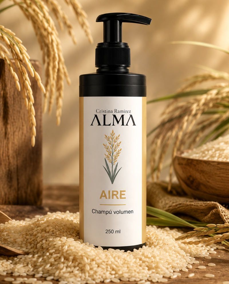 Botella de champú ALMA Aire sobre granos de arroz, con tallos de trigo en un entorno de color beige cálido.