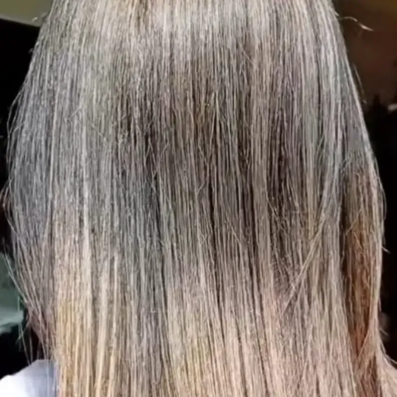 Primer plano de cabello largo y liso con raíces grises visibles y puntas rubias.