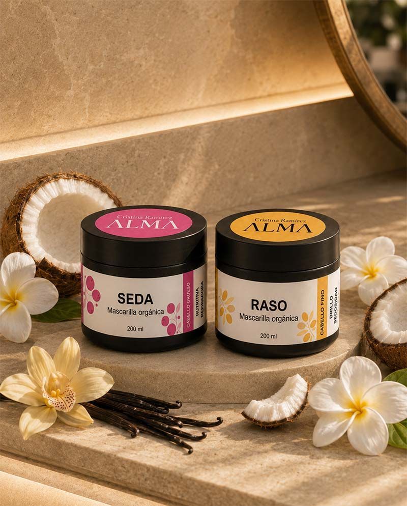 Dos frascos perfumados etiquetados como SEDA y RASO con flores y vainas de vainilla sobre una superficie beige.