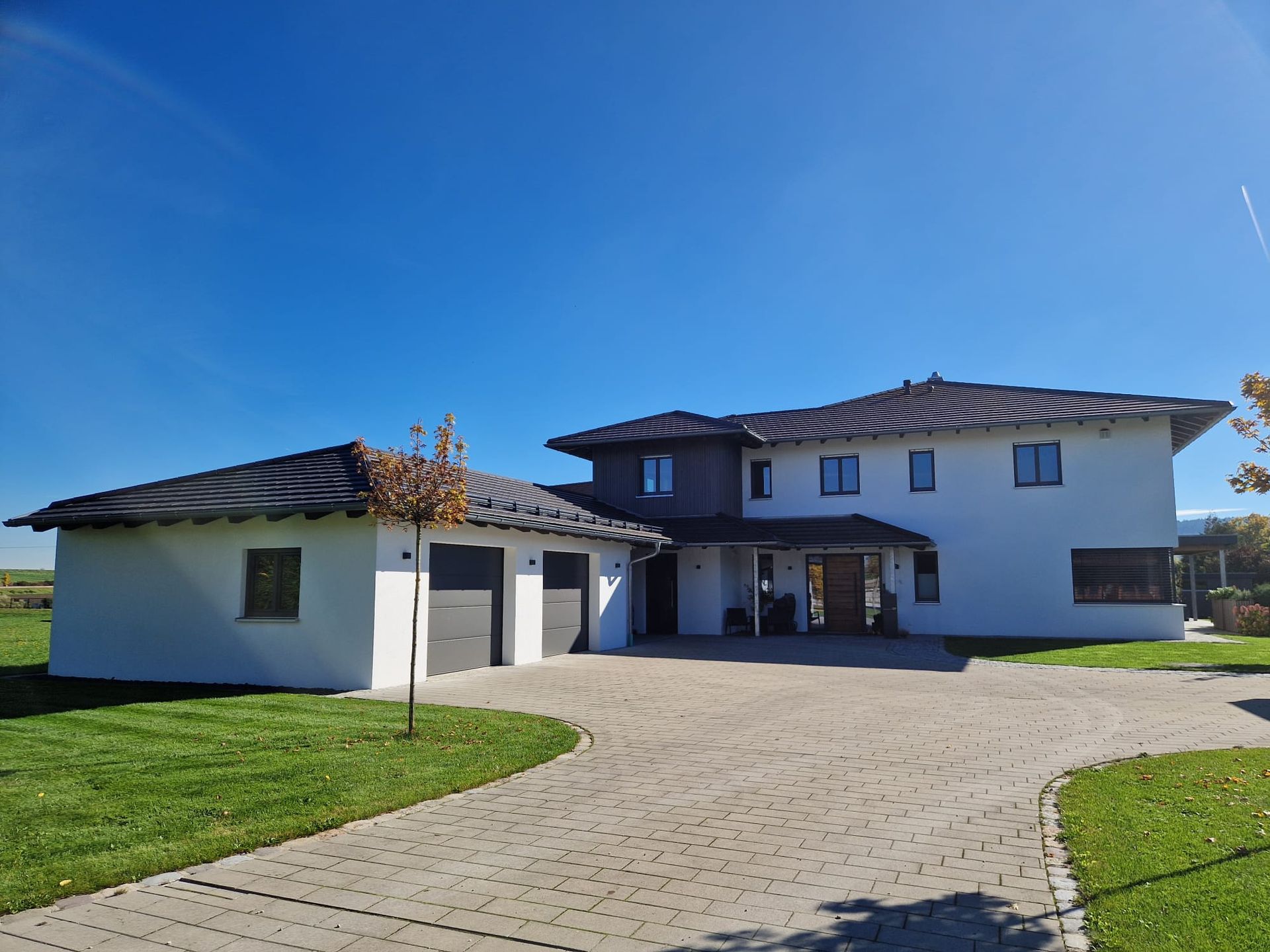 Modernes Haus mit weißer Fassade, angeflachtem Dach und zwei Garagen