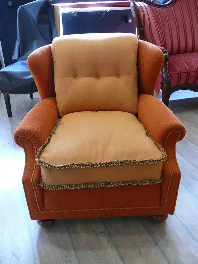 Orange-brauner Polstersessel mit geknöpfter Rückenlehne und detaillierter Verzierung, im Kontrast zu anderen Möbeln.