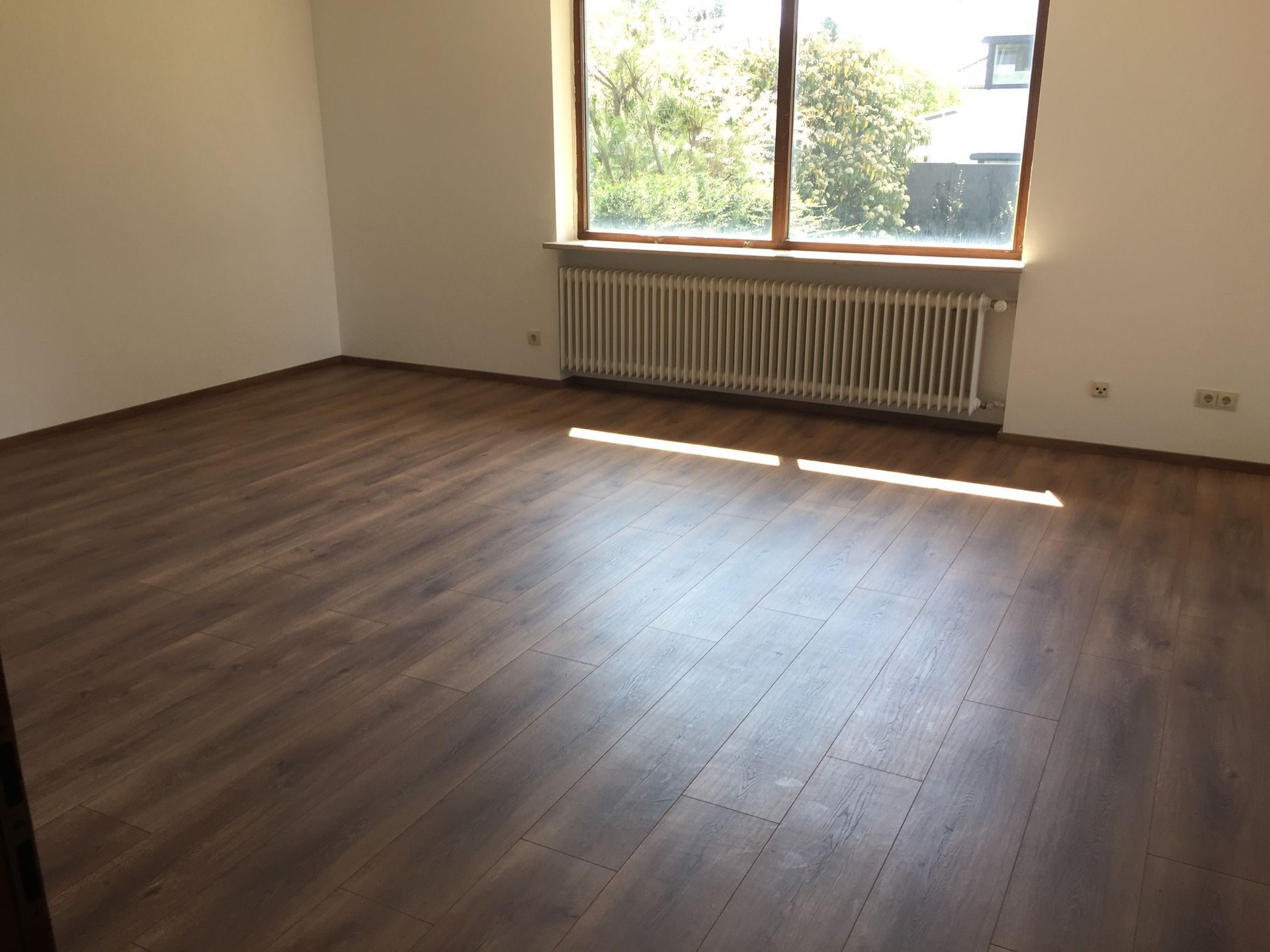 Person mit orangefarbenen Handschuhen beizt Holzbretter mit einer Rolle und verwendet dabei eine Schale mit brauner Beize.