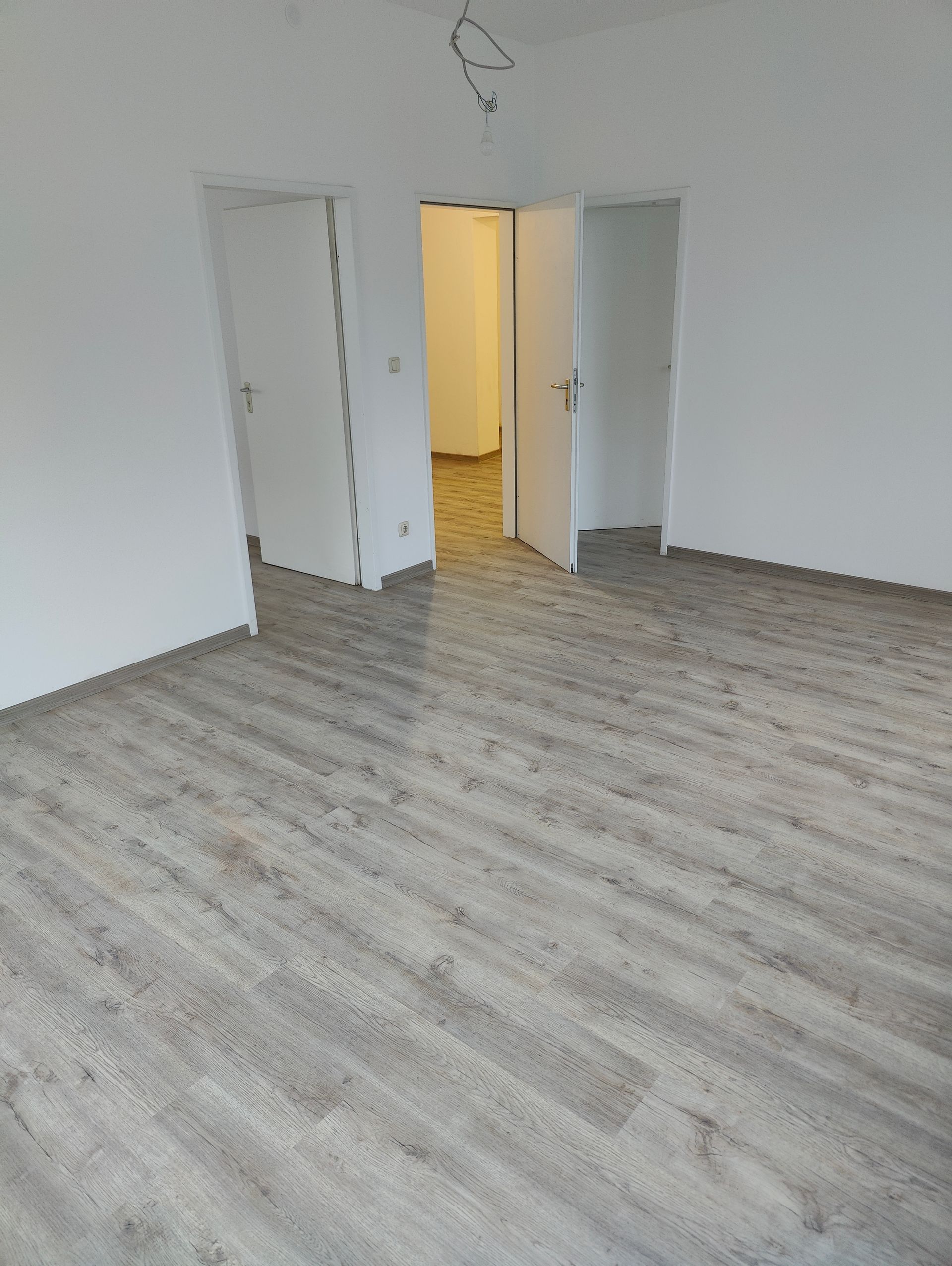 Zwei Personen in Schutzanzügen reinigen einen Raum mit Wasserschaden. Einer hält eine Plane und der andere untersucht ein Fenster.