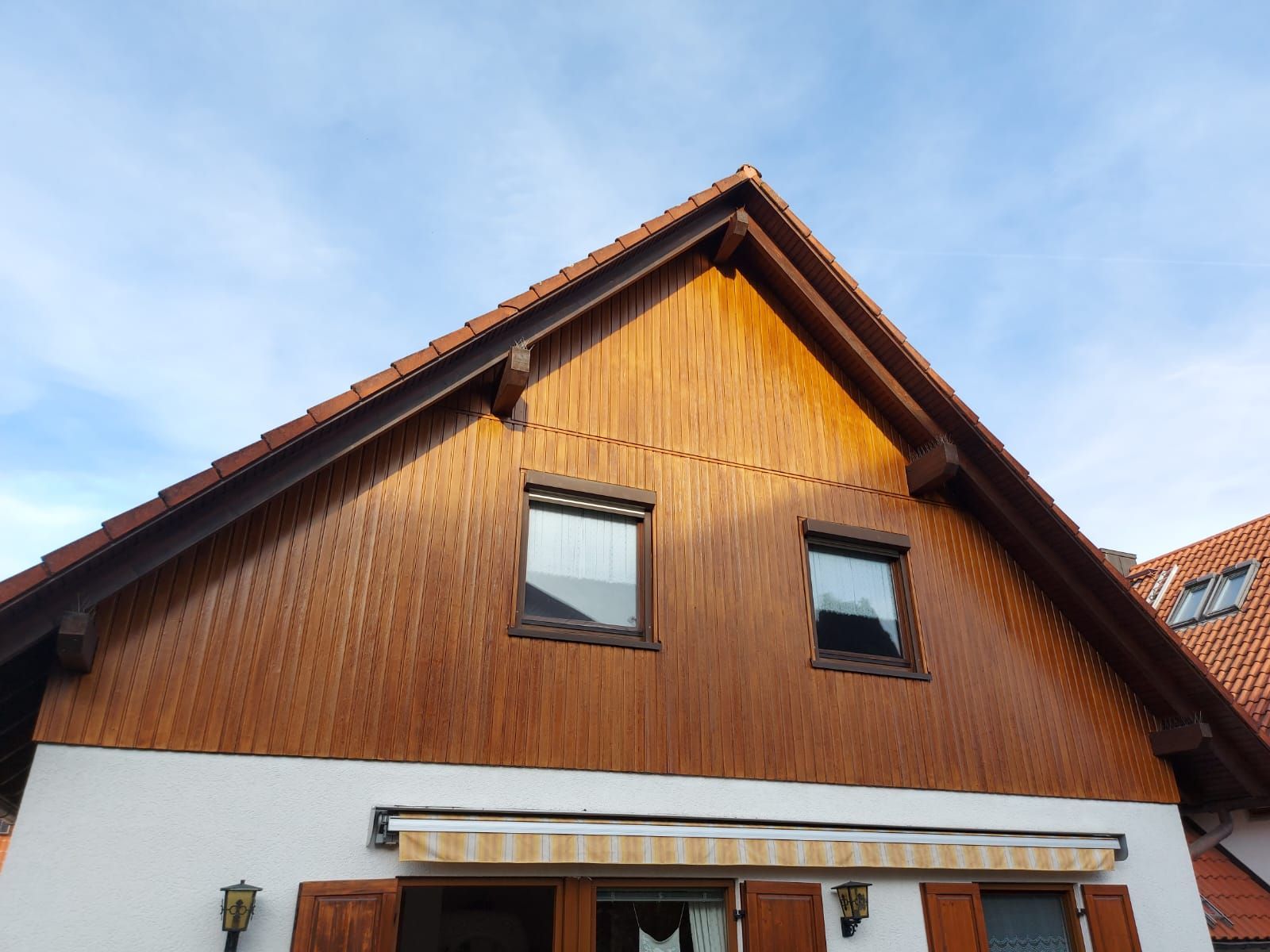 Person mit orangefarbenen Handschuhen beizt Holzbretter mit einer Rolle und verwendet dabei eine Schale mit brauner Beize.