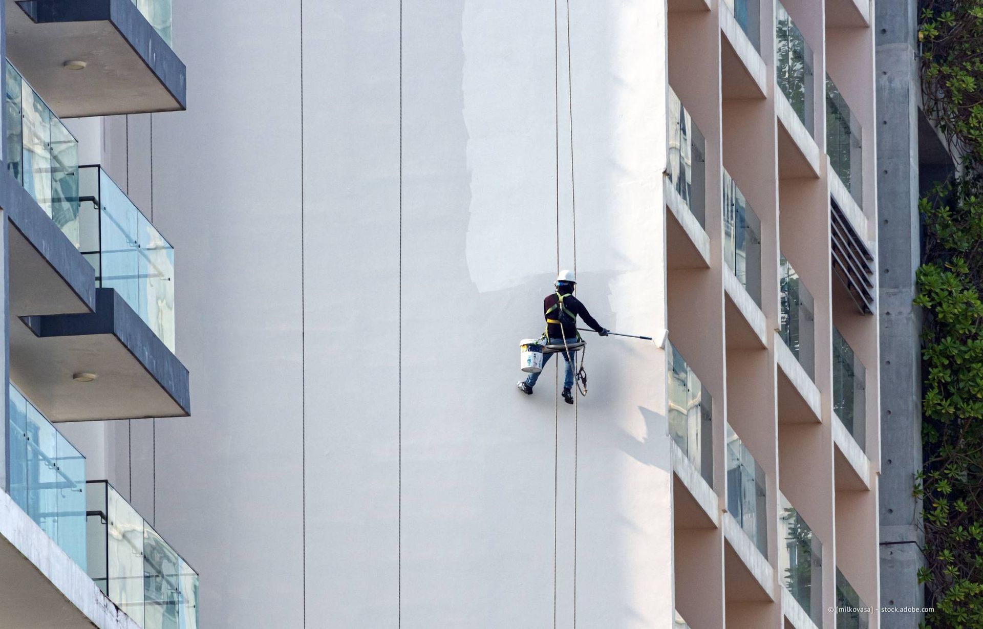 Ein Arbeiter, der an Seilen hängt, streicht die Außenfassade eines Hochhauses.