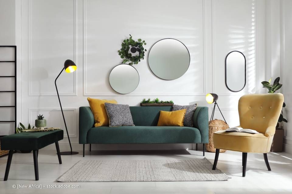 Grünes Sofa und gelber Sessel in einem weißen Raum mit Spiegeln und einer schwarzen Stehlampe.