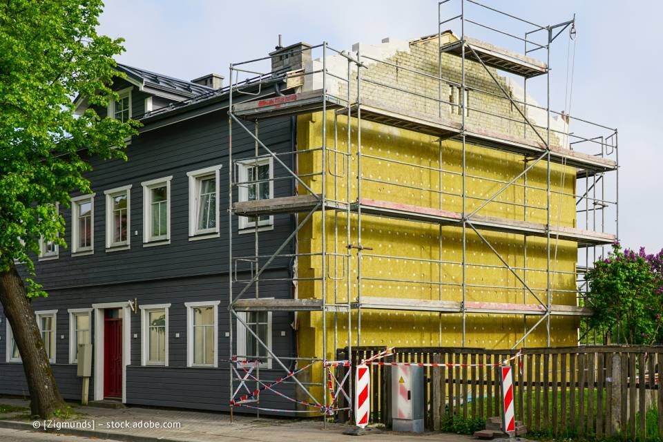 Gebäude wird renoviert, an der Seite sind Gerüst und Isolierung sichtbar.