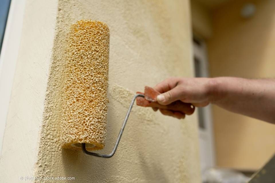 Person, die mit einer Spezialrolle Strukturfarbe auf eine Außenwand aufträgt.