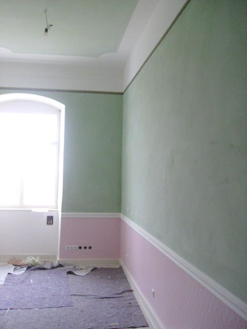 Grünes Sofa und gelber Sessel in einem weißen Raum mit Spiegeln und einer schwarzen Stehlampe.