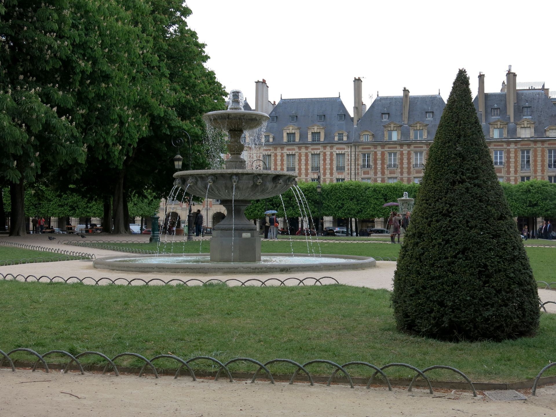 Château historique entouré d'un jardin bien entretenu avec une fontaine et des arbres taillés en forme conique.