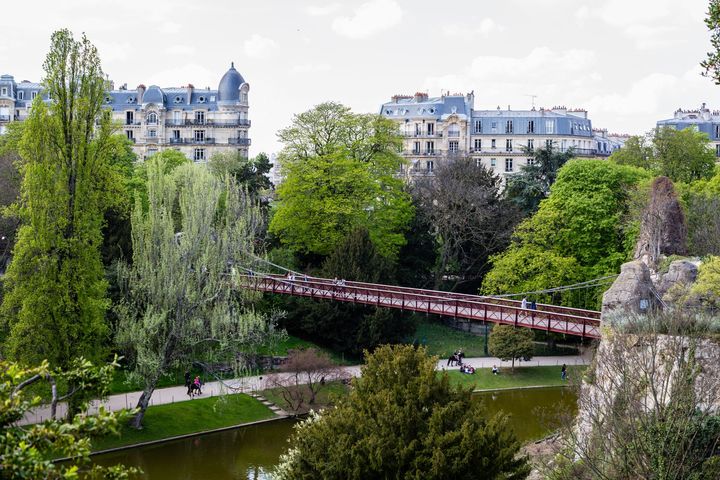 Vue panoramique d'un parc urbain avec un pont et des bâtiments historiques en arrière-plan.