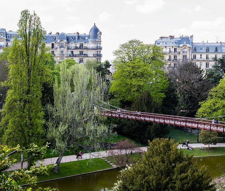 Vue d'un parc urbain avec un pont et des arbres verdoyants.
