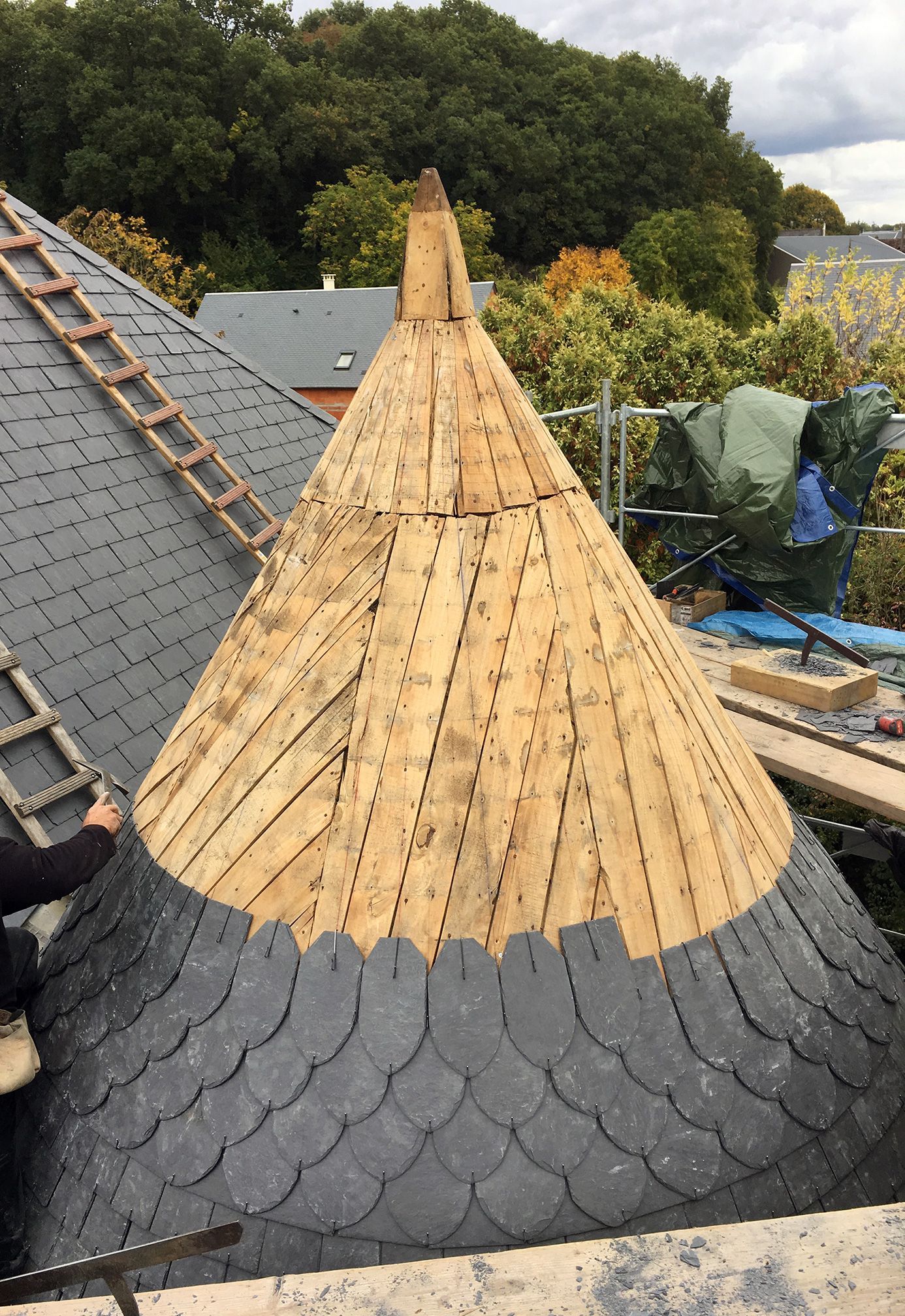 Professionnel mettant des tuiles en ardoise sur une tour d'un toit atypique.