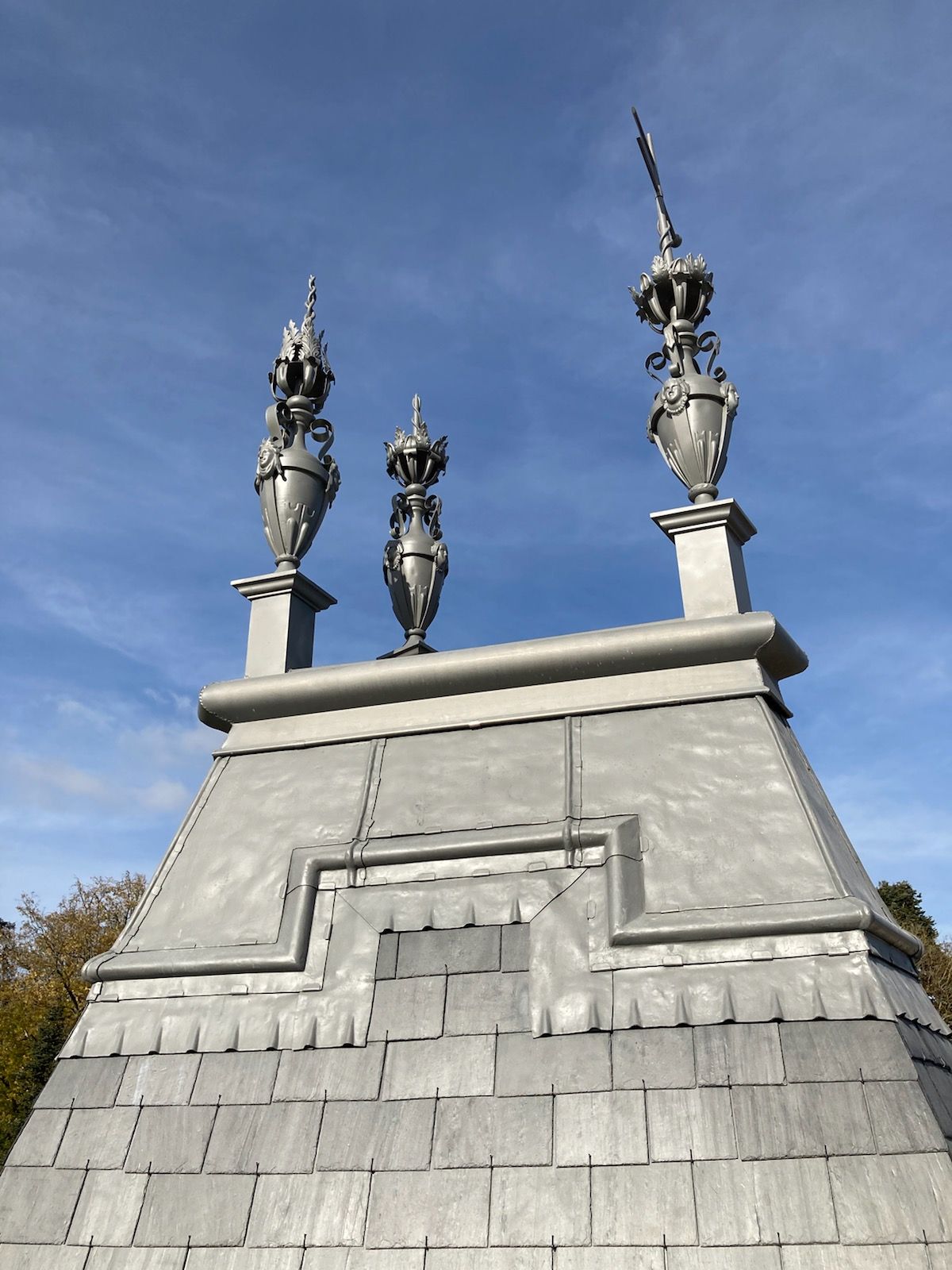 Trois piliers avec vases sur la partie haute d'une toiture.