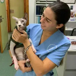 Una mujer con un uniforme azul sostiene un gato en sus brazos.