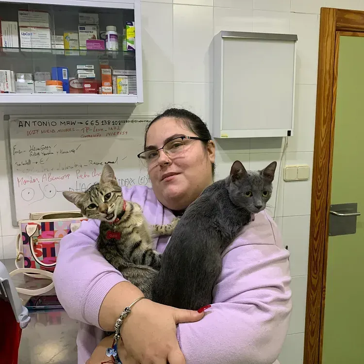 Una mujer sostiene dos gatos en sus brazos.