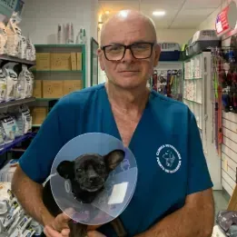Un hombre con un uniforme azul sostiene un perro con un cono en la cabeza.