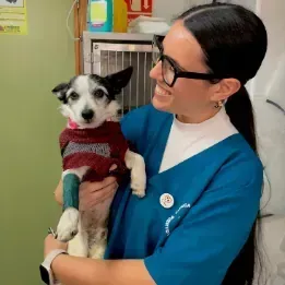 Una mujer sostiene en sus brazos un pequeño perro blanco y negro.
