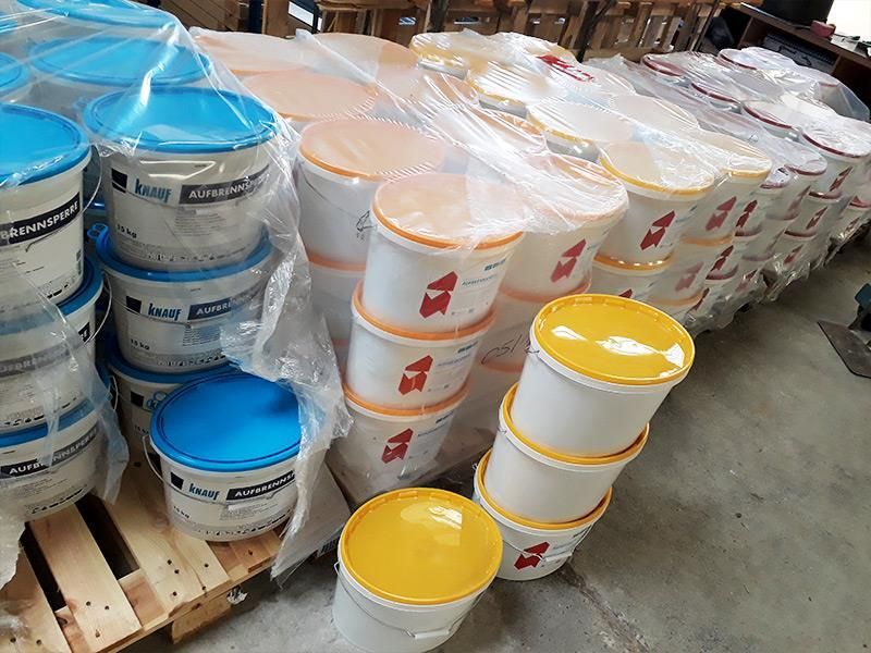 Auf einer Holzpalette sind Farbeimer übereinander gestapelt.