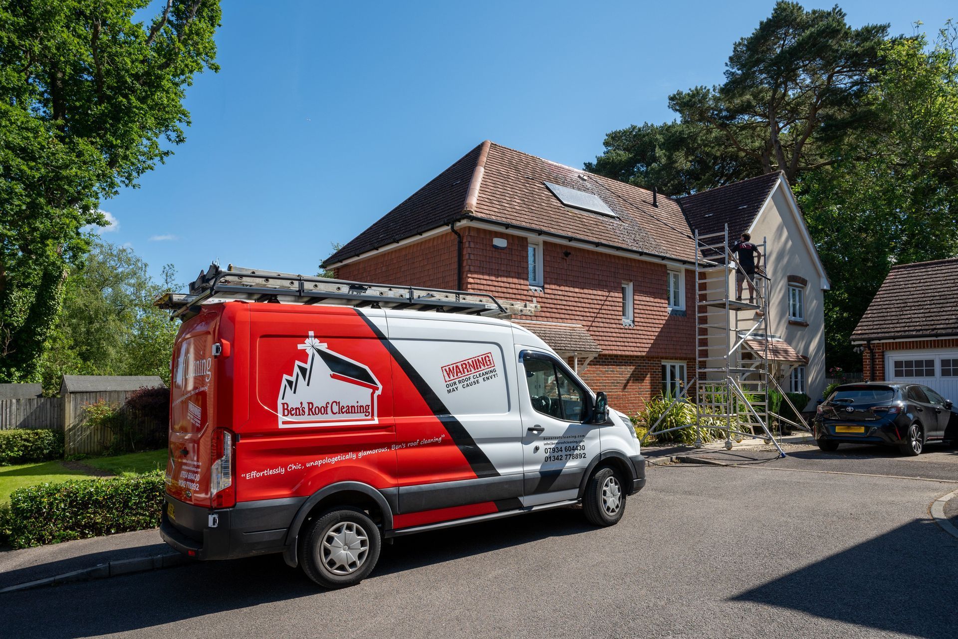 Red and white delivery van parked outside a brick house on a sunny residential street.
