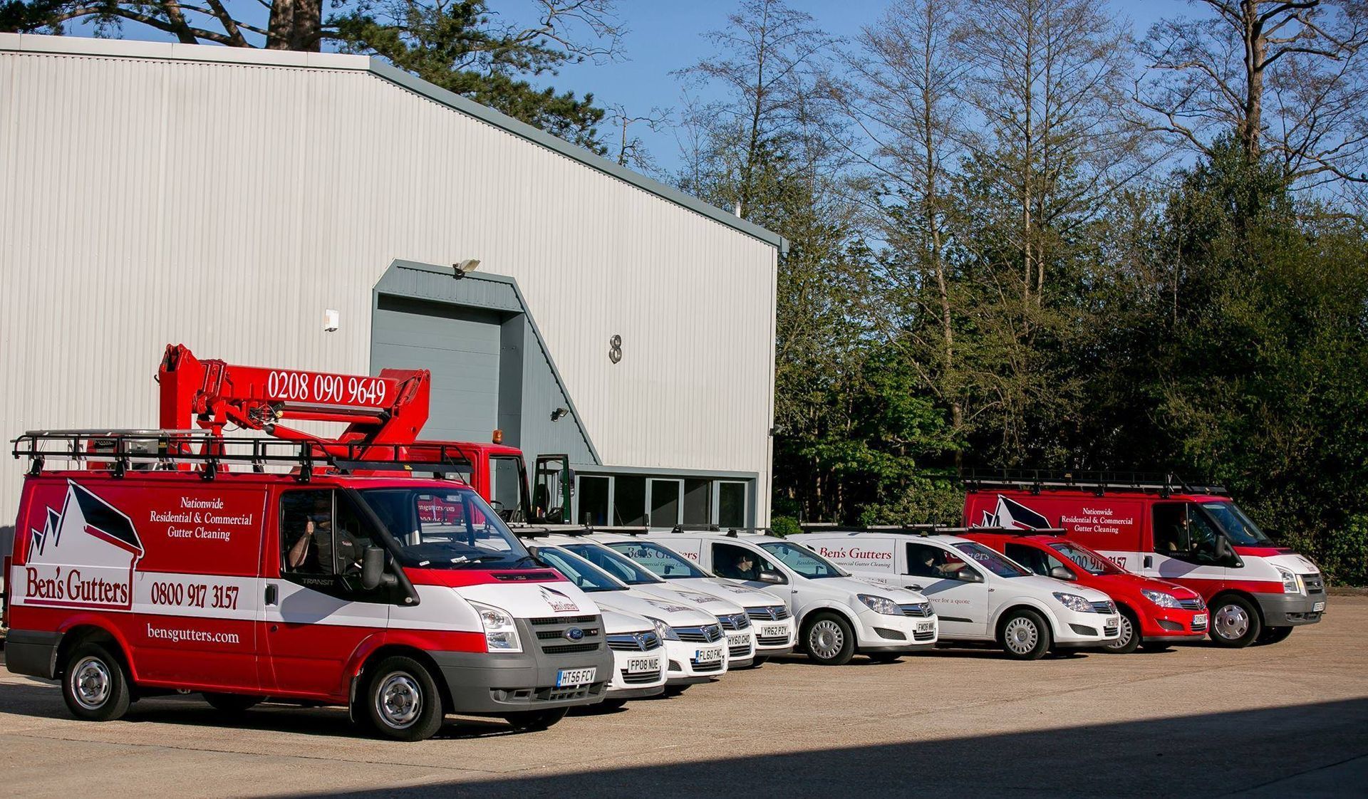Red-and-white rescue vehicles and white vans parked outside a large industrial building