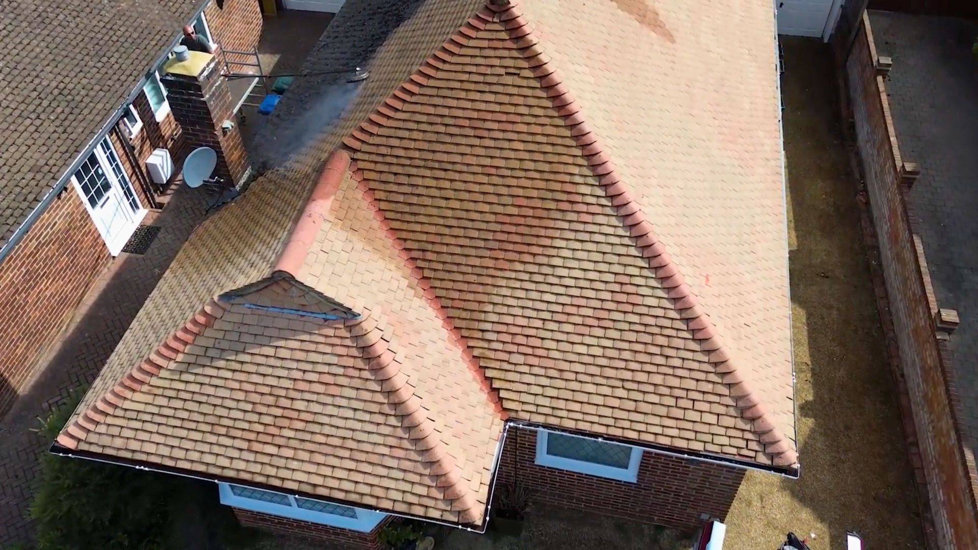 Aerial view of a red-tiled roof on a house beside a driveway and neighboring homes.