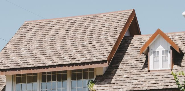 House roof with brown shingles and white dormer windows against a blue sky
