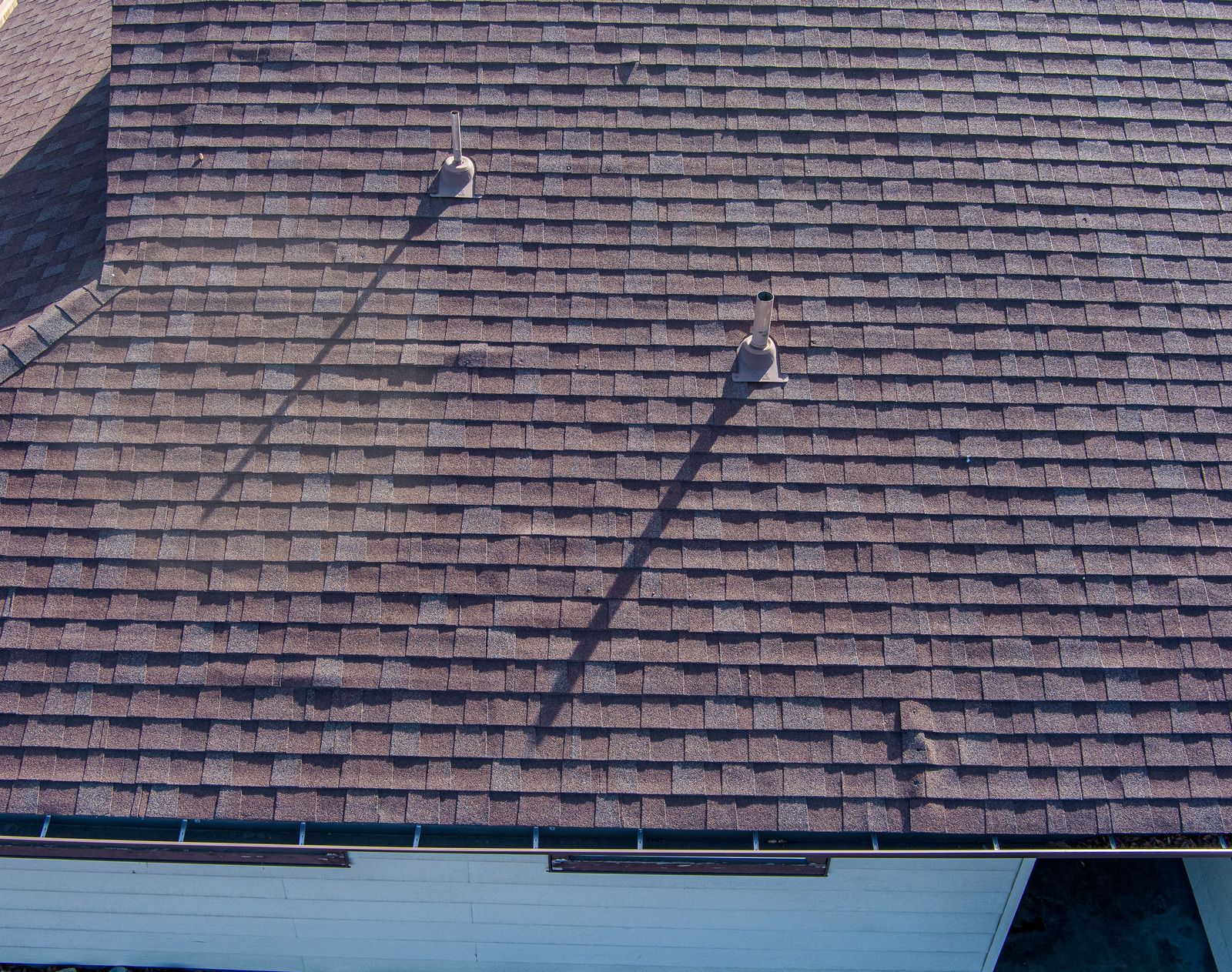 Shingled roof with two vents casting long shadows in bright sunlight
