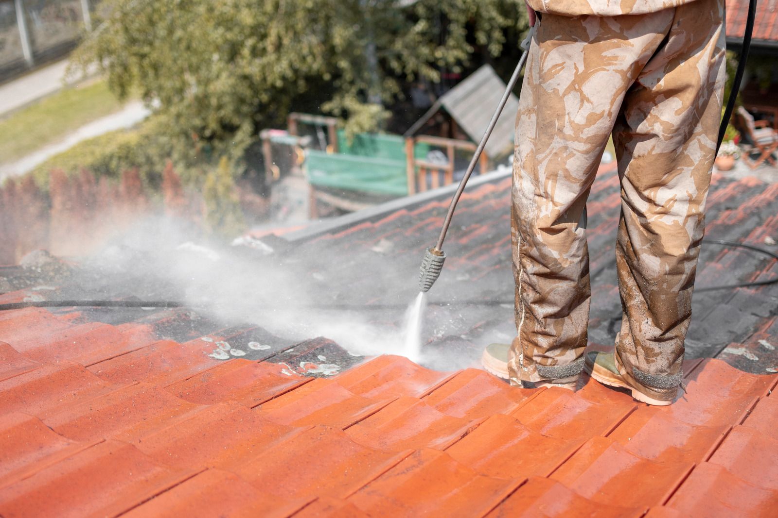 Worker pressure-washing a red roof with water spray visible