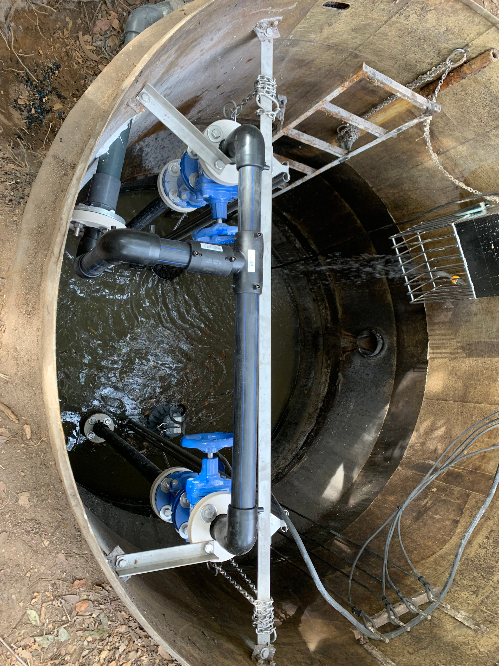 Un regard avec une échelle au-dessus est rempli d'eau et de tuyaux.