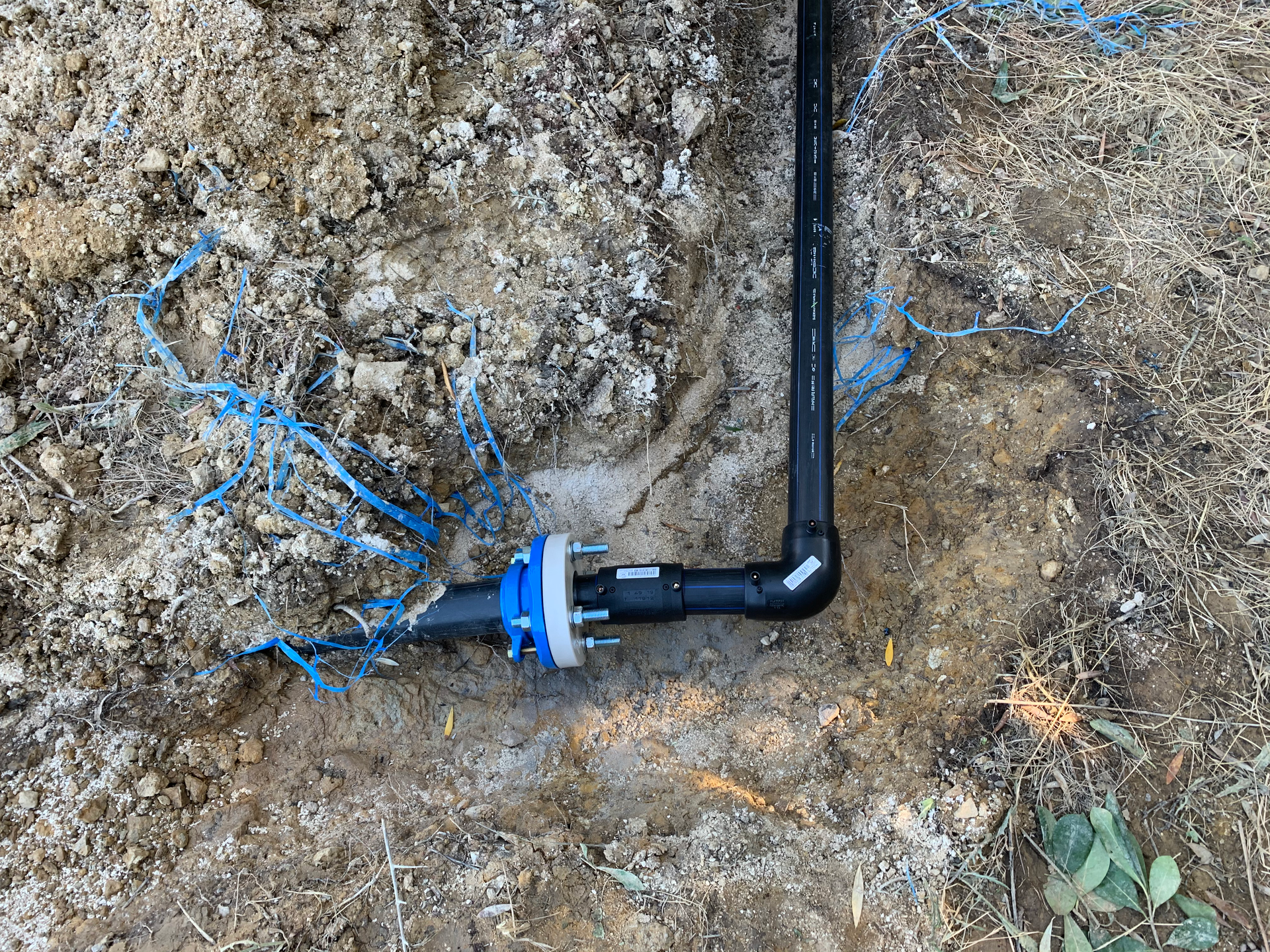 Un tuyau noir repose dans la terre à côté d'un tuyau bleu.