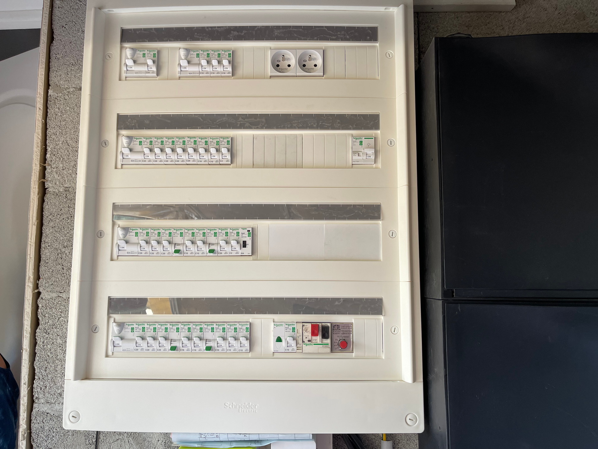 Un boîtier électrique blanc avec un réfrigérateur noir en arrière-plan