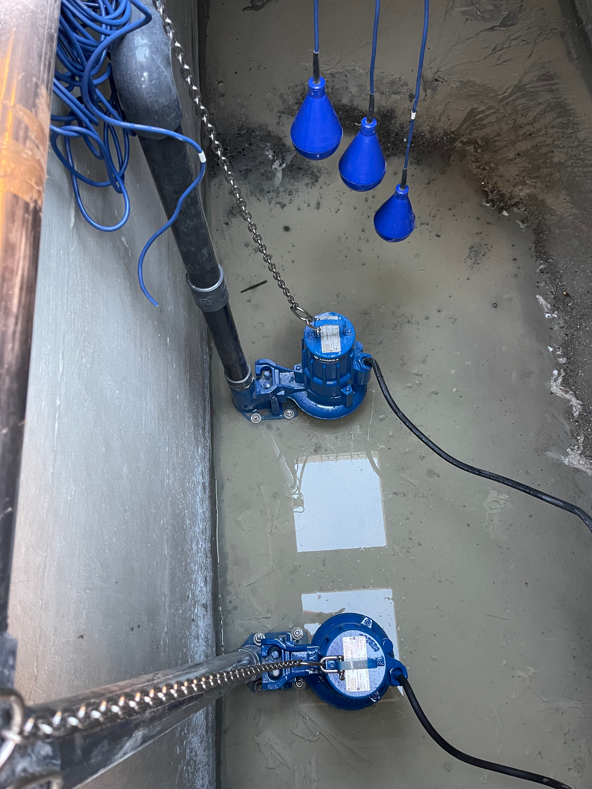 Trois pompes bleues sont reliées à une chaîne dans une chambre en béton.