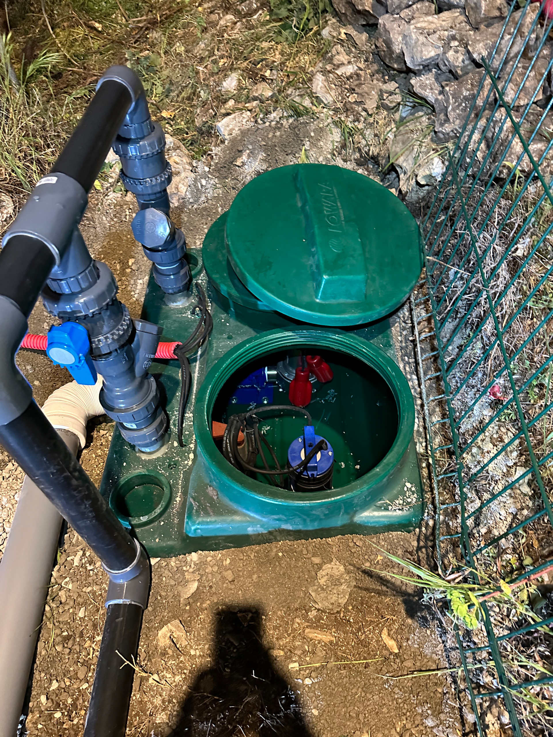 Une boîte verte avec le couvercle ouvert est posée sur le sol à côté d'une clôture.